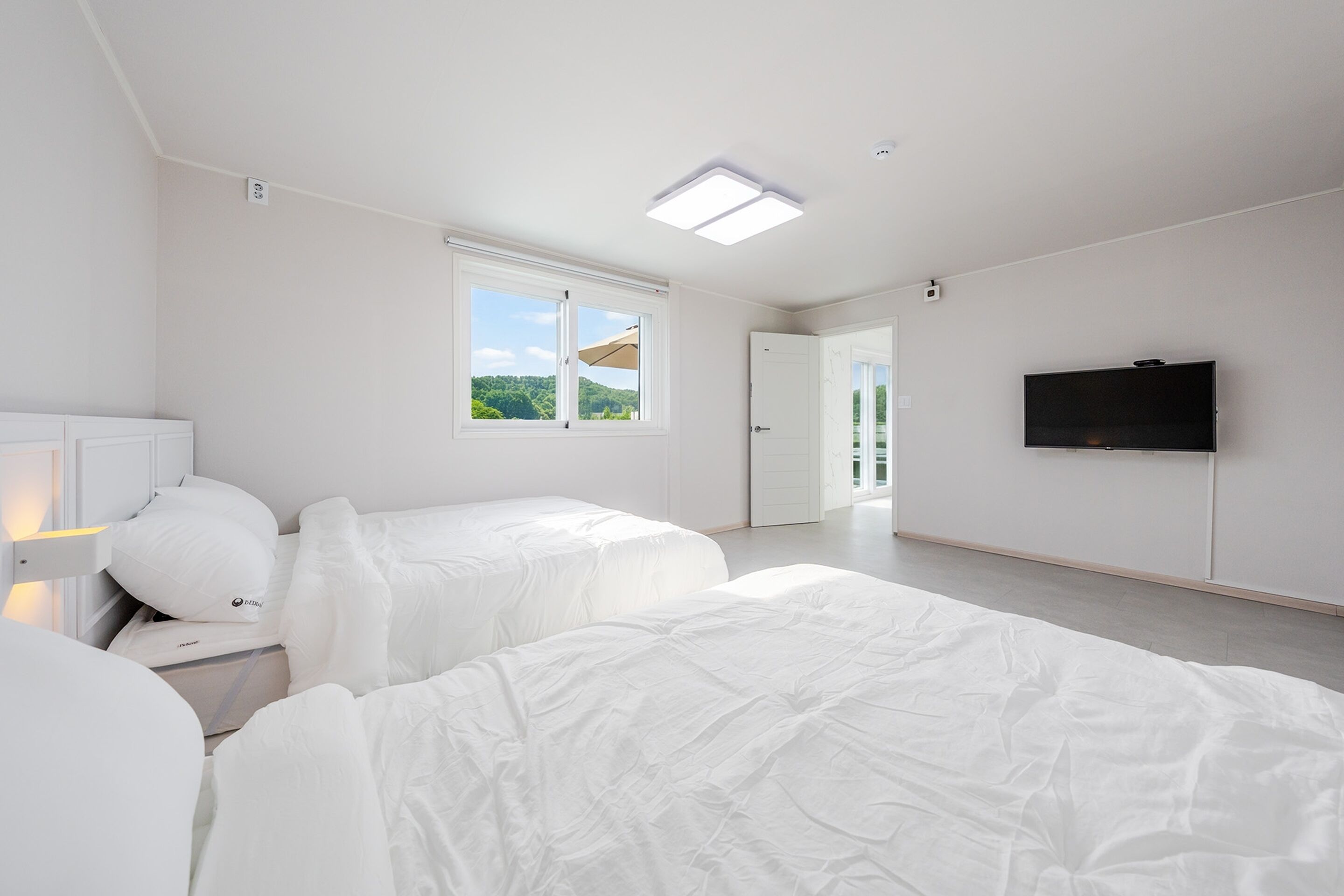 A hotel room with two beds, a TV, a window with a view, and a door leading to another room.