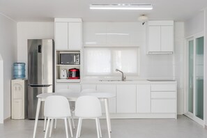 Una cocina moderna con armarios blancos, un refrigerador de acero inoxidable, un microondas y un dispensador de agua.