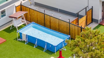 Et rektangulært swimmingpool med blå poolafdækning, omgivet af et træhegn og en græsplæne.