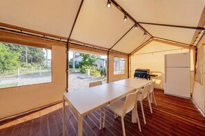 Una habitación tipo tienda de campaña con una mesa de comedor, sillas, un refrigerador y una parrilla.
