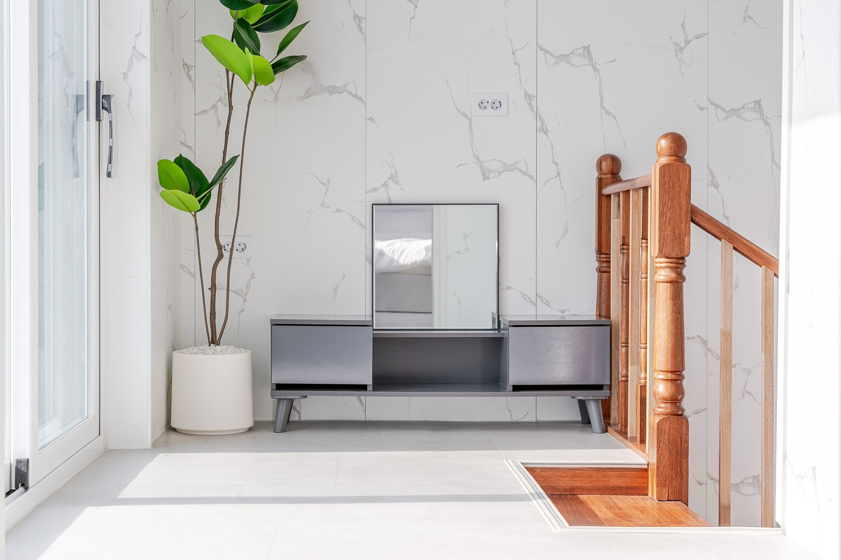 Une salle de bain moderne avec un mur en marbre, une plante en pot, un miroir et un escalier en bois.
