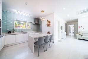 A modern kitchen with a central island, white cabinetry, and a view of the outdoors. - Gangneung Ujin Pool Villa (Gangneung)