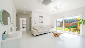 Una sala de estar moderna con un sofá, una mesa de centro de vidrio y vista a un patio trasero con un tobogán.