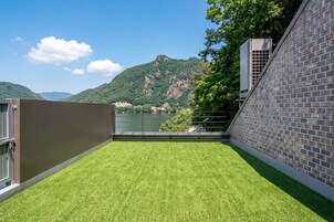 A rooftop terrace with a view of a lake and mountains, a brick wall, and a metal railing.