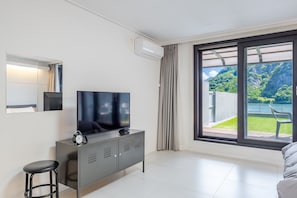 Una habitación de hotel moderna con un ventanal grande, un televisor de pantalla plana, un minibar y un taburete pequeño.