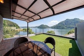 A terrace with a view of a lake and hills, furnished with wicker chairs and a glass table.