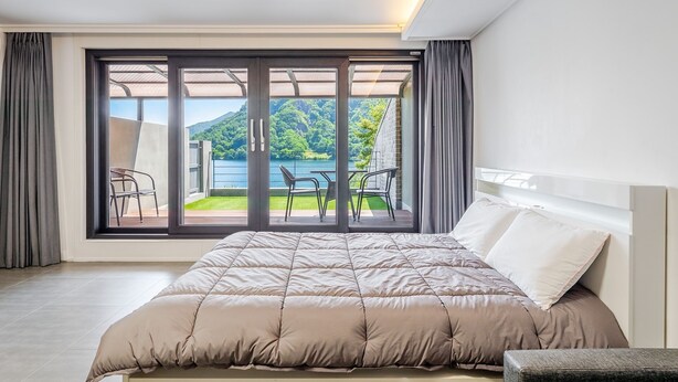 A bedroom with a bed, a view of a balcony with chairs, and a large window. - Chuncheon Rabbit Star Pension (Chuncheon)