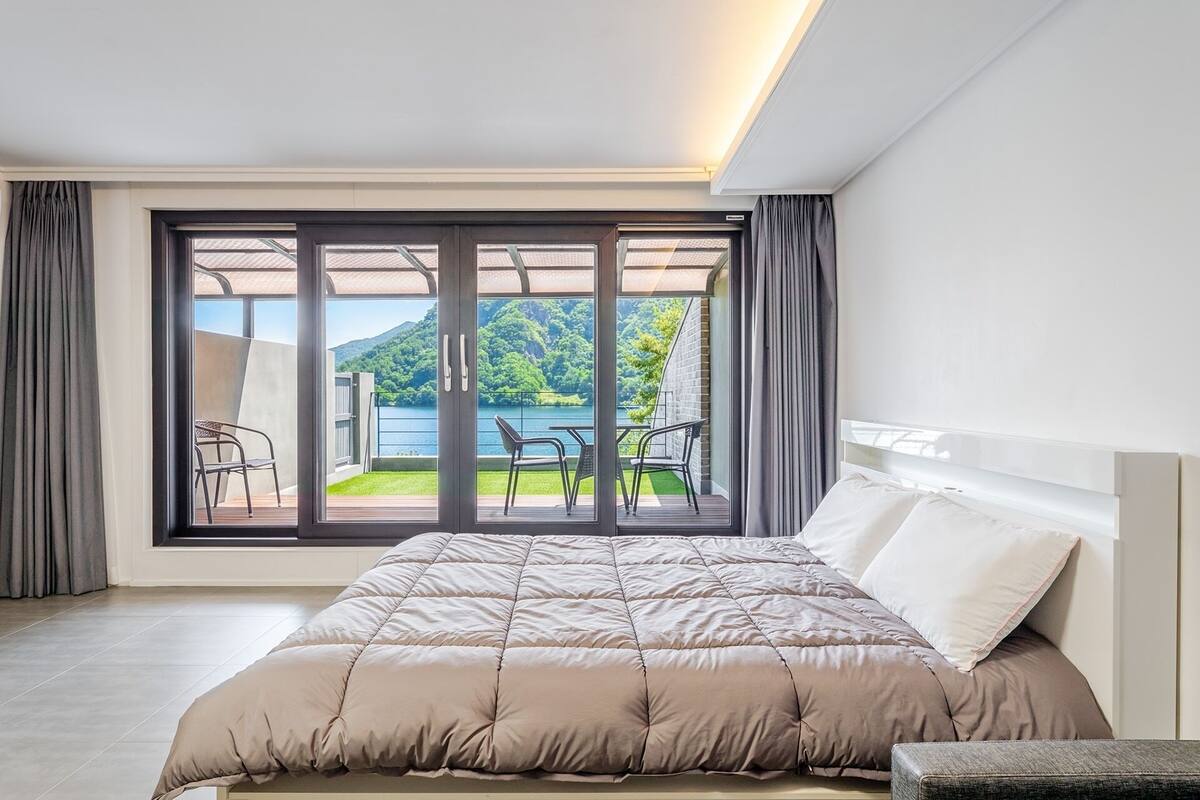 Un dormitorio con cama, vistas a un balcón con sillas y un ventanal grande.