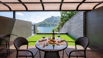 A dining area with a table set for two, overlooking a mountain and a body of water.