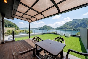 A covered outdoor seating area with a table and chairs, overlooking a lake and hills.