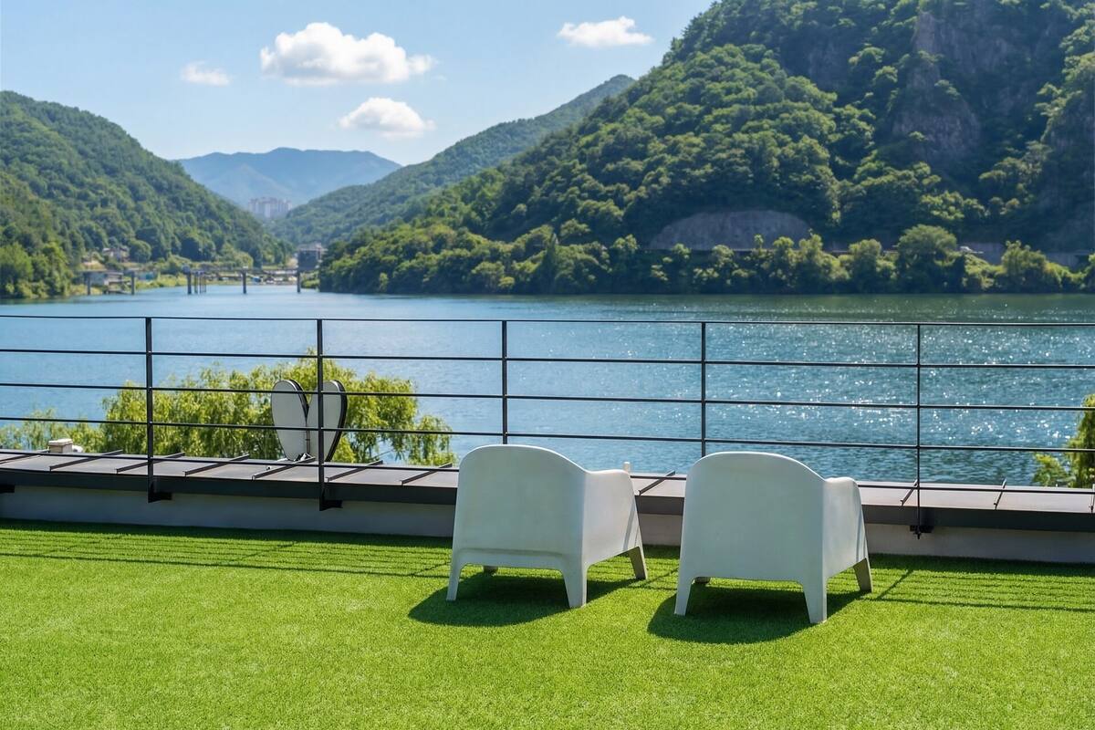 Una terraza con dos sillas blancas, una barandilla y vistas a un lago rodeado de colinas.