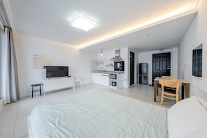 A modern bedroom with a large bed, a TV, a small kitchen area, and a dining table.