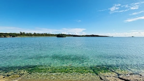 A clear view of a calm sea with a rocky shoreline and distant land. - Uruma Dome Okinawa Saturn7 (Uruma)