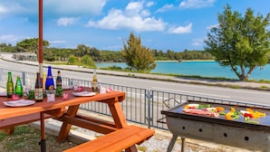 A picnic setup with a grill, table, and bottles, overlooking a body of water and a road. - Uruma Dome Okinawa Saturn7 (Uruma)