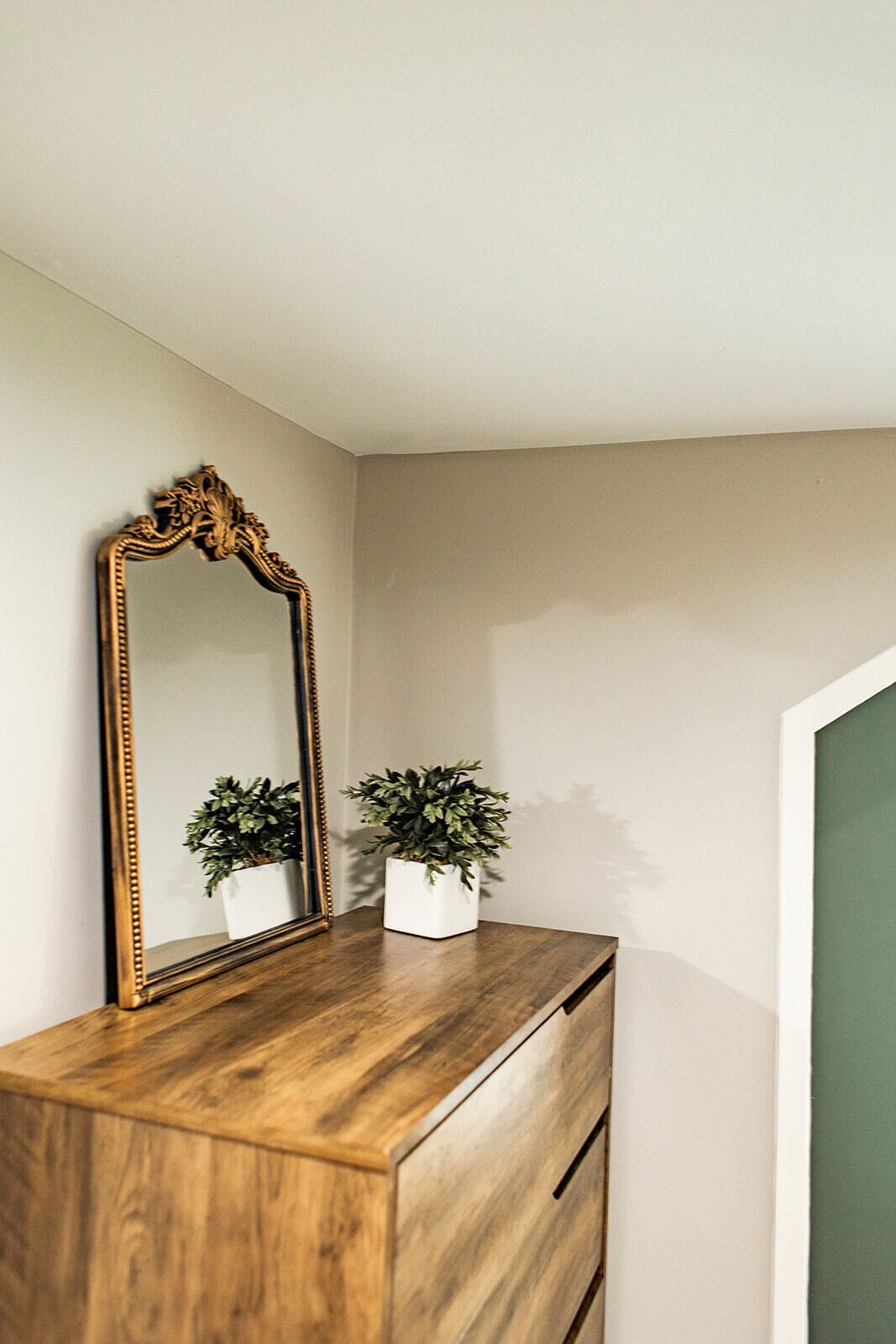 Een houten dressoir met een grote, versierde spiegel en twee potplanten.