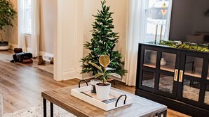 Een woonkamer met een houten bijzettafeltje, een plant in pot, een televisie en een open haard.