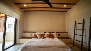 Un dormitorio con una cama grande, un ventilador de techo, una escalera y vistas a través de un ventanal.