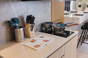 A modern kitchen with a gas stove, a cutting board, and a set of knives. - Premium Apartment by Kozystay - Antasari Place (Kota Jakarta Selatan)