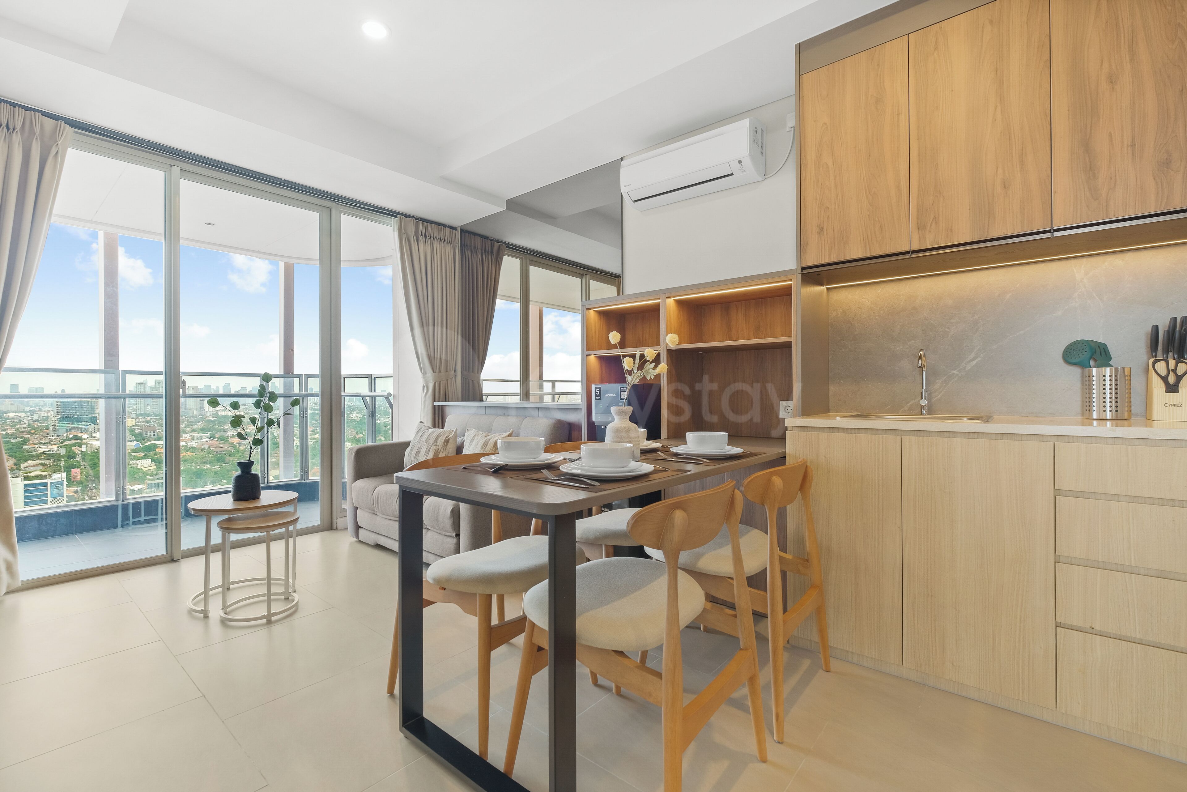 Una cocina moderna con armarios de madera, una zona de comedor con mesa y sillas, y un ventanal con vistas a la ciudad.
