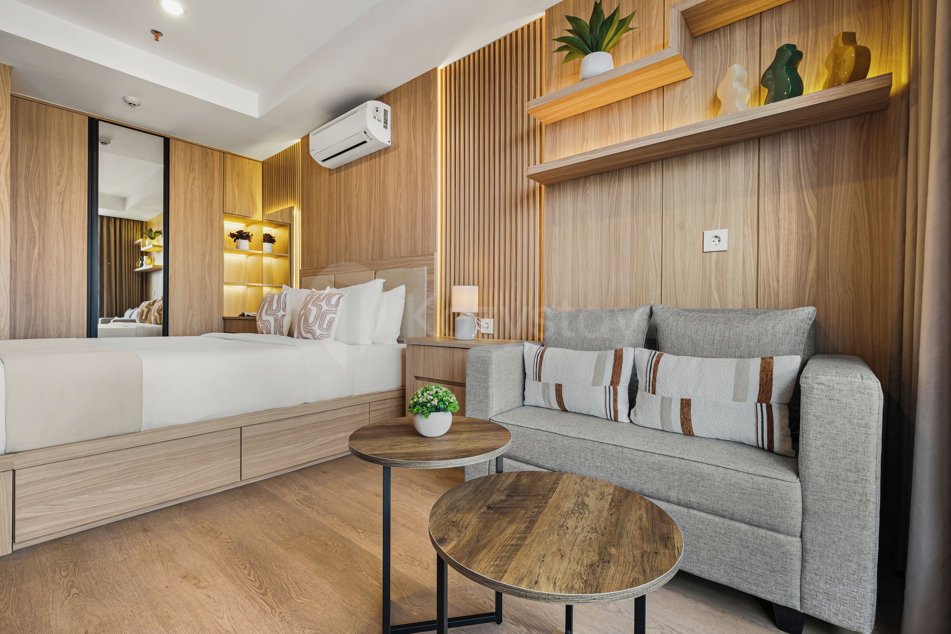 Una habitación de hotel moderna con cama, sofá, una mesa redonda y estanterías empotradas.