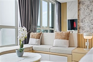 A modern hotel room with a sofa, a small table, a potted plant, and a lamp. - Premium Apartment by Kozystay - Antasari Place (Kota Jakarta Selatan)