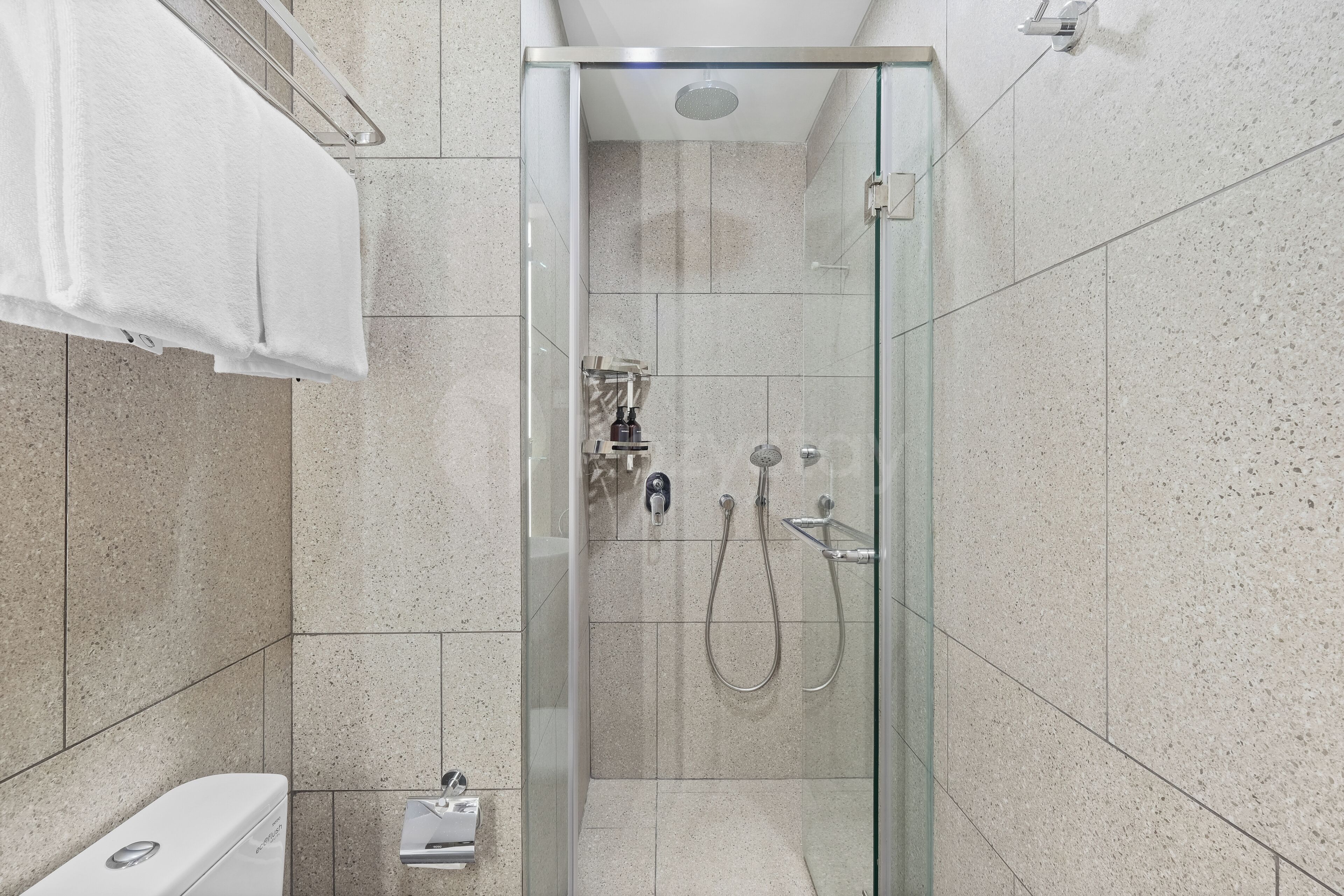 Cabina de ducha con paredes de vidrio, un cabezal de ducha de mano y un grifo empotrado.