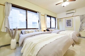 Une chambre d’hôtel avec deux lits, un ventilateur de plafond, un appareil de climatisation et une fenêtre avec des rideaux.
