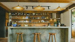 Una cocina con barra, taburetes de madera, lámparas colgantes y un respaldo de ladrillo.