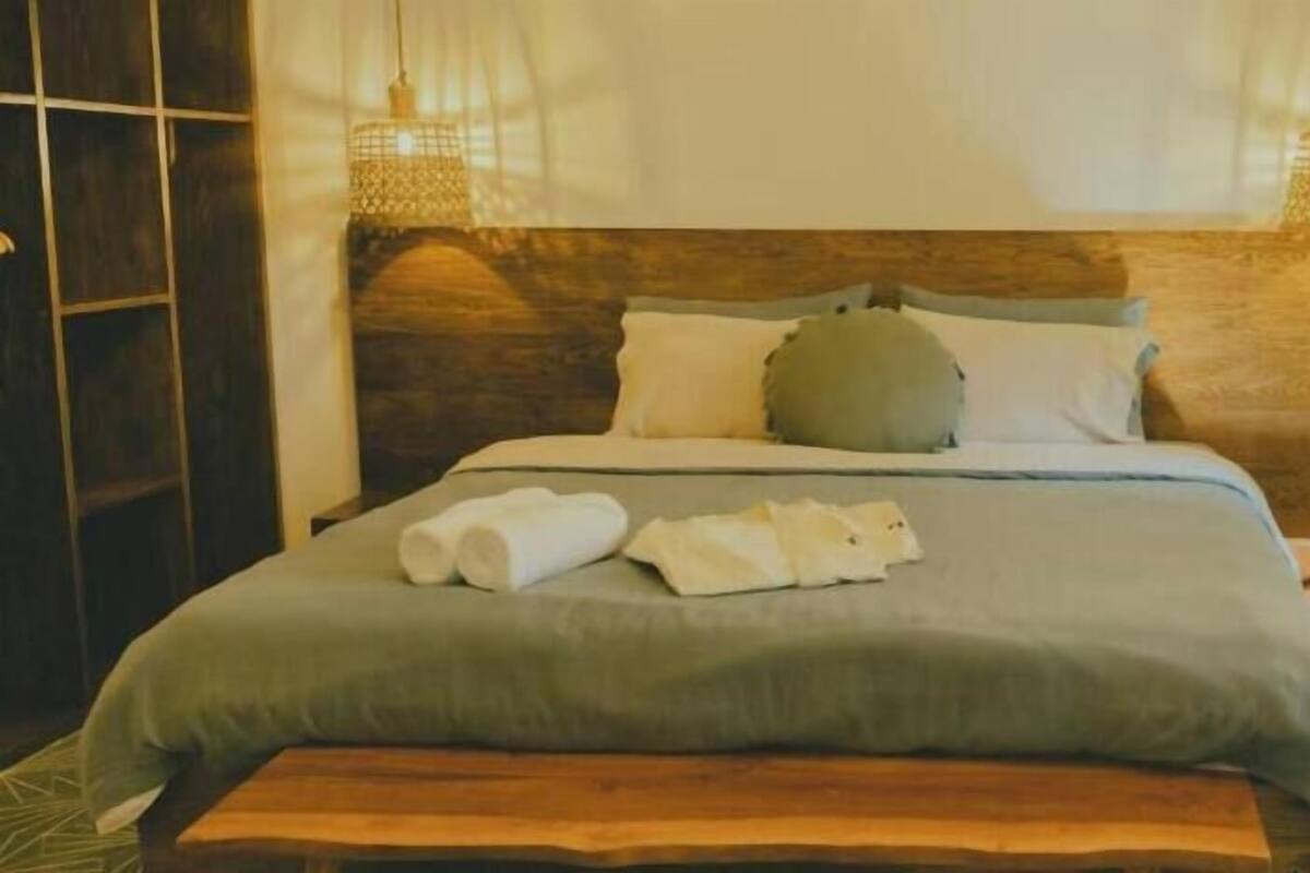 A neatly made bed with a wooden headboard, a bedside table, and a hanging light fixture.