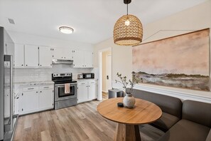 Una cocina moderna con armarios blancos, electrodomésticos de acero inoxidable, una mesa redonda de madera y un cuadro abstracto grande en la pared.