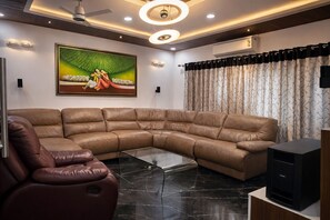 A modern living room with a sectional sofa, a leather armchair, a glass coffee table, and a flat-screen TV.
