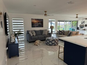 A modern living room with a grey sofa, a coffee table, a dog lying on the floor, and a large window with blinds. - 3-bedroom house in pleasant Port Charlotte with cool AC (Port Charlotte)