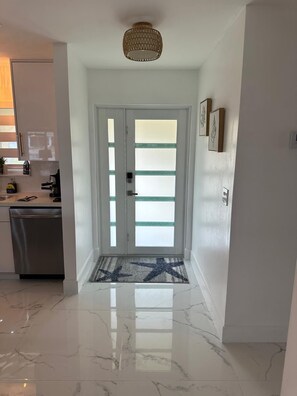 A hallway with a double door, a doormat, a ceiling light fixture, and a kitchen area with a dishwasher. - 3-bedroom house in pleasant Port Charlotte with cool AC (Port Charlotte)