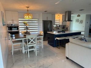 A modern kitchen with white cabinetry, a central island, a dining area with white chairs, and a sofa. - 3-bedroom house in pleasant Port Charlotte with cool AC (Port Charlotte)