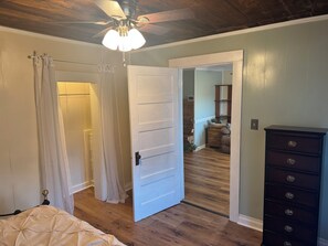 Ein Schlafzimmer mit einem Bett, einem Deckenventilator, einer Tür zu einem anderen Raum und einer Kommode.