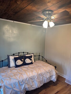 Un dormitorio con cama, ventilador de techo y suelo de madera.