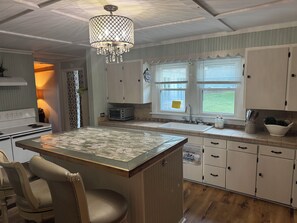Una cocina con una isla central, muebles blancos, un microondas y una araña.