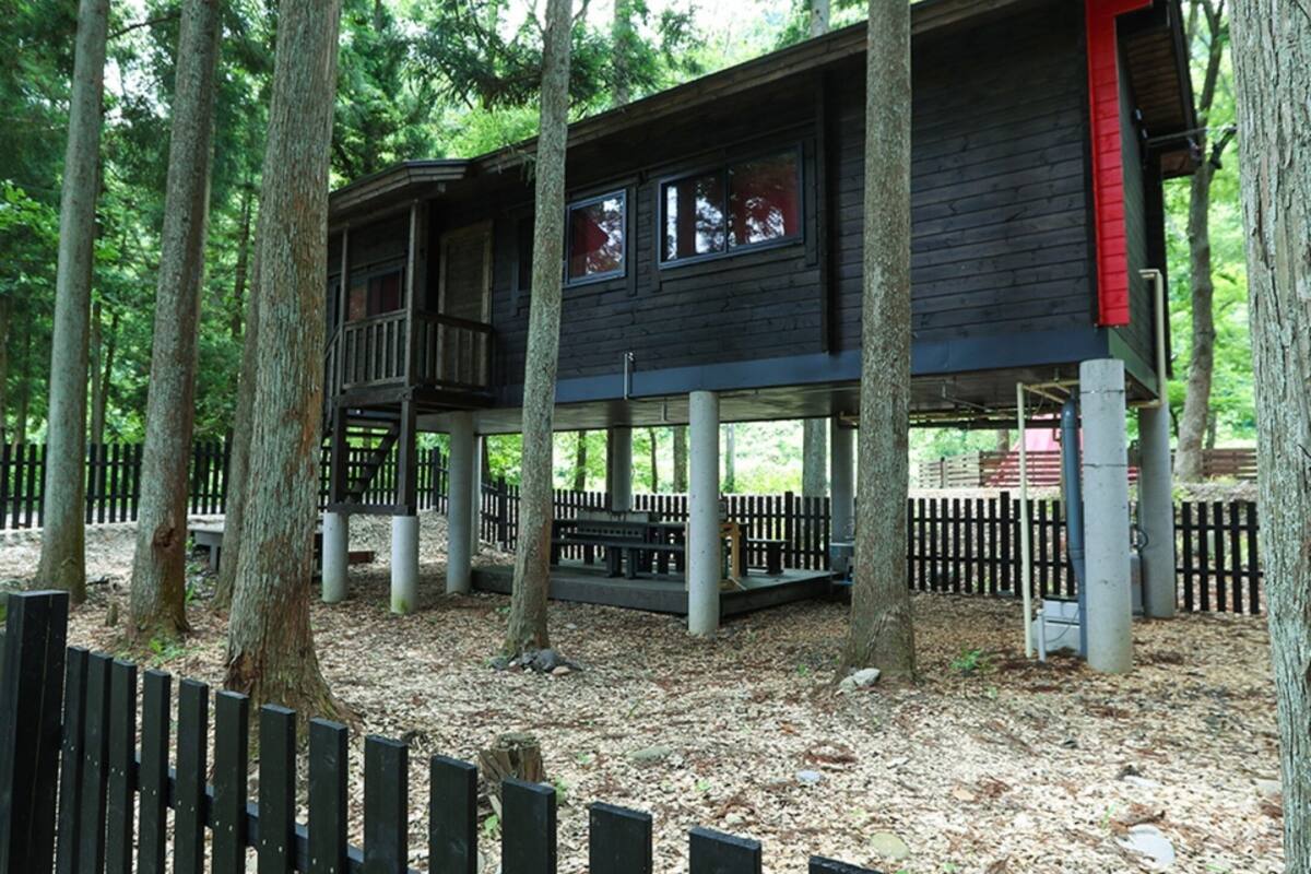 A wooden cabin with a balcony, surrounded by trees and a wooden fence.