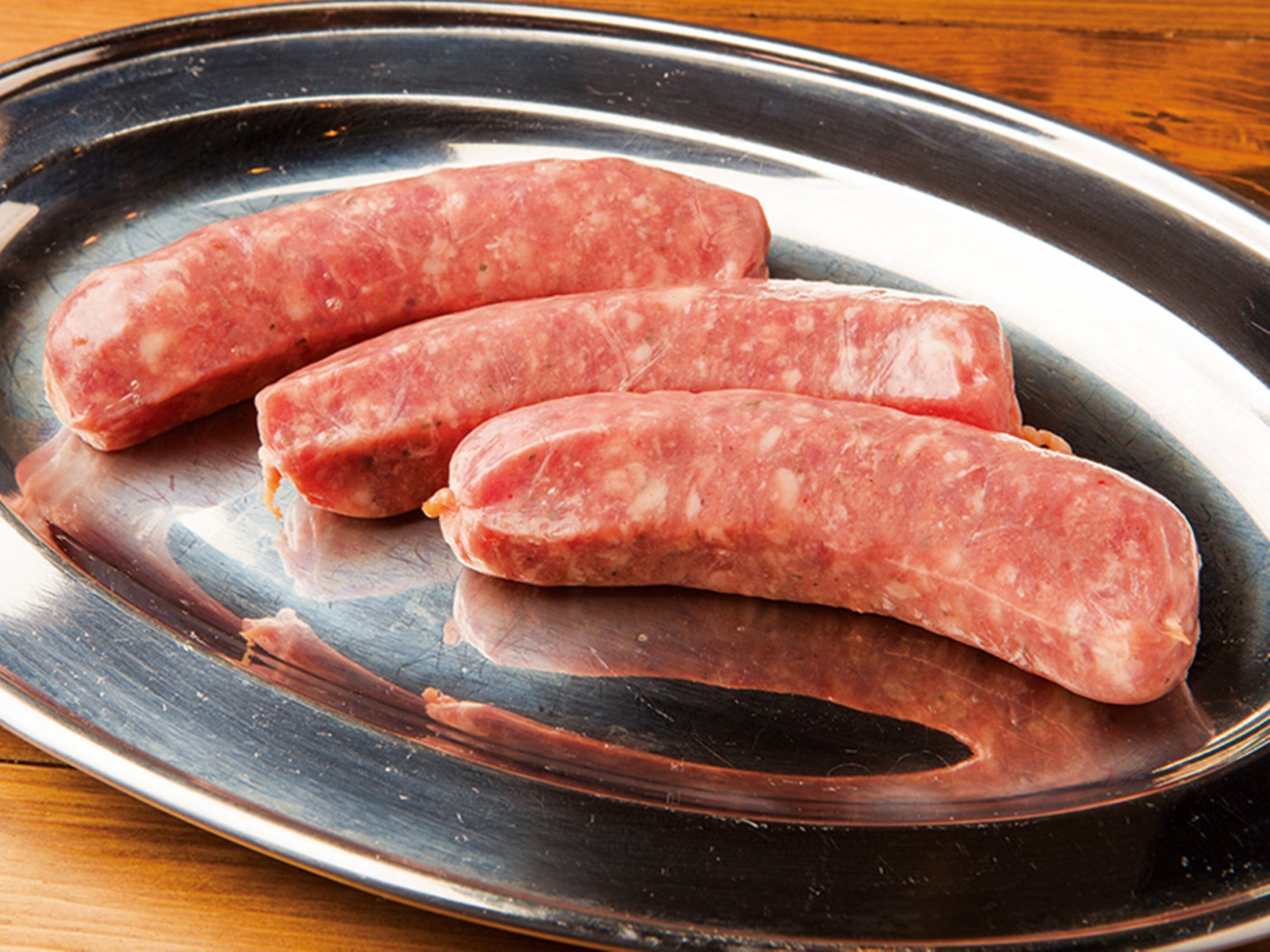 Tres salchichas crudas sobre un plato de acero inoxidable.