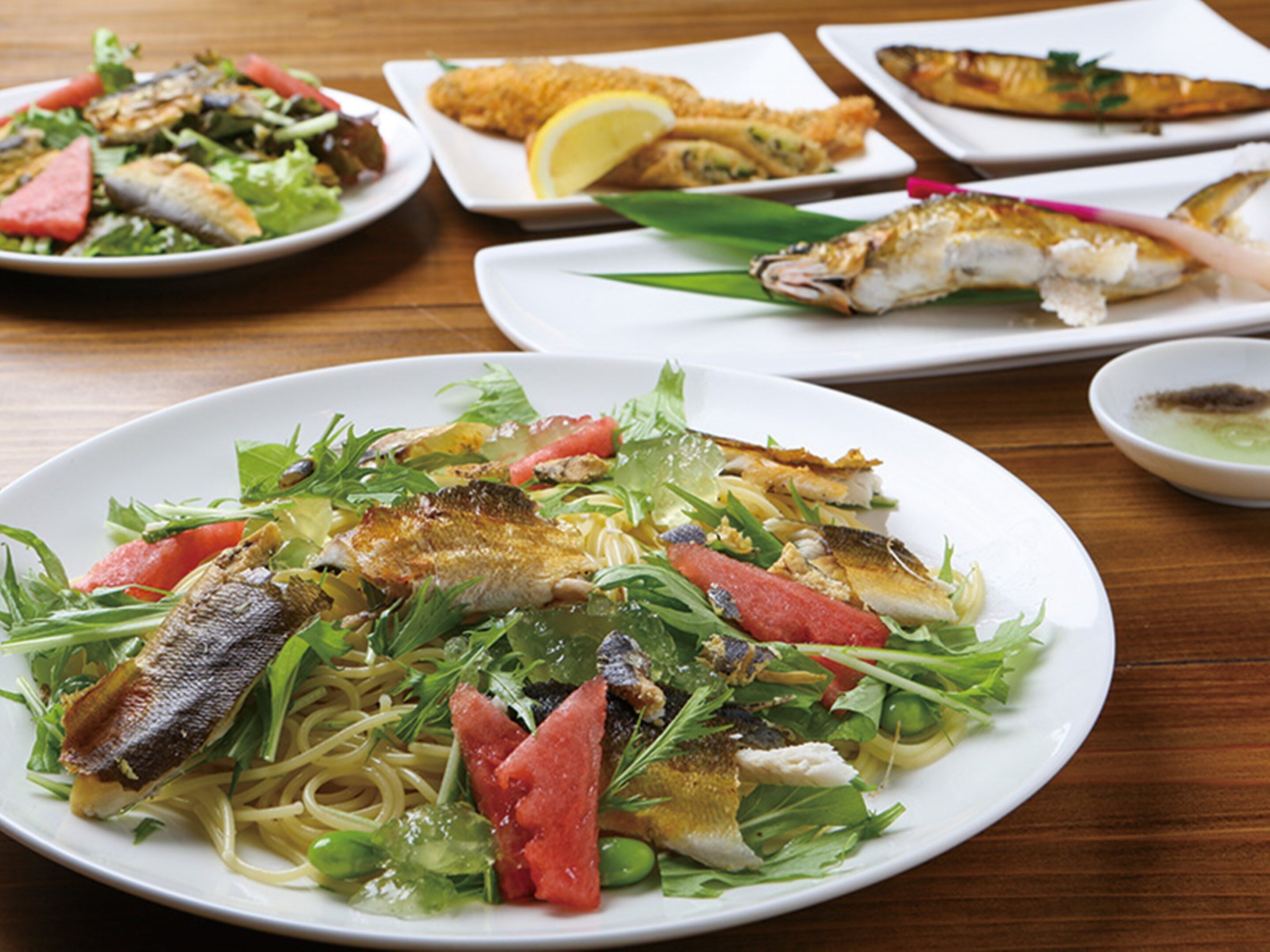Ein Tisch mit verschiedenen Speisen, darunter Pasta mit Fisch und Gemüse sowie weitere angerichtete Gerichte.