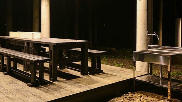 An outdoor patio with a wooden table and benches, a metal sink, and a concrete pillar. - Nagomiya Seseragi (Gujo)