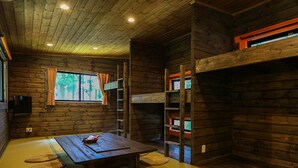 A wooden cabin interior with a tatami mat floor, a table with a basket, a window with curtains, and a bunk bed. - Nagomiya Seseragi (Gujo)