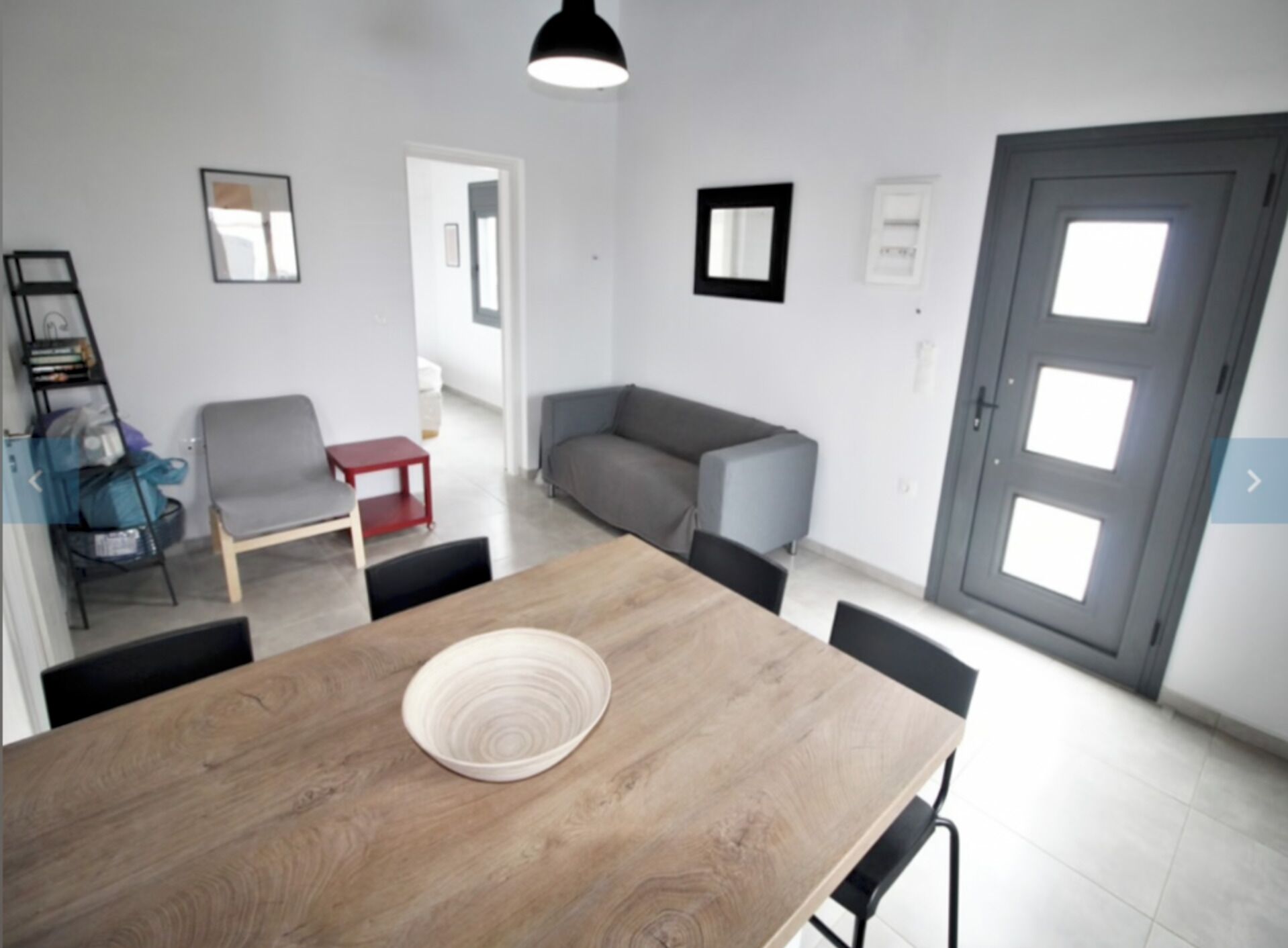 A modern living room with a wooden dining table, a grey sofa, and a red side table.