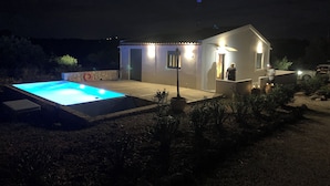 Una pequeña casa con piscina, un muro de piedra e iluminación exterior.