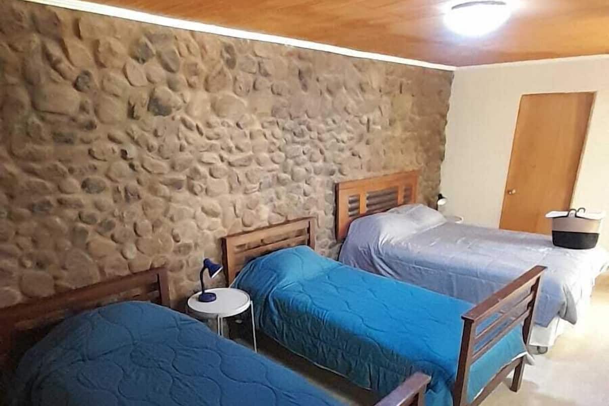 Una habitación con dos camas de madera, un muro de piedra y suelo de baldosas.