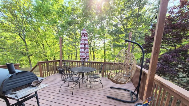 Eine Holzterrasse mit Grill, einem runden Tisch, Stühlen und einer Hängematte.