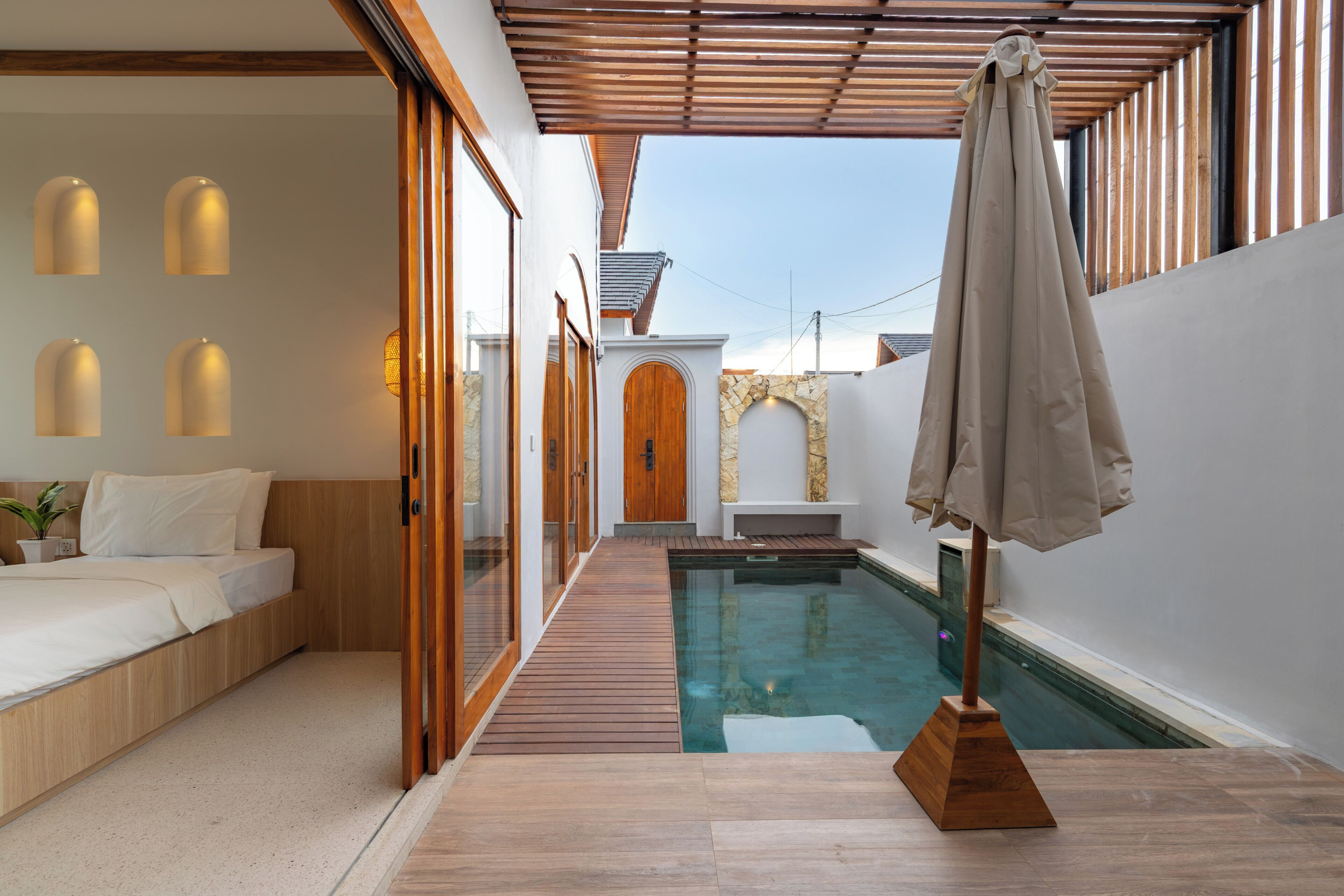 A modern room with a wooden floor, a bed, a small pool, and a pergola with an umbrella.