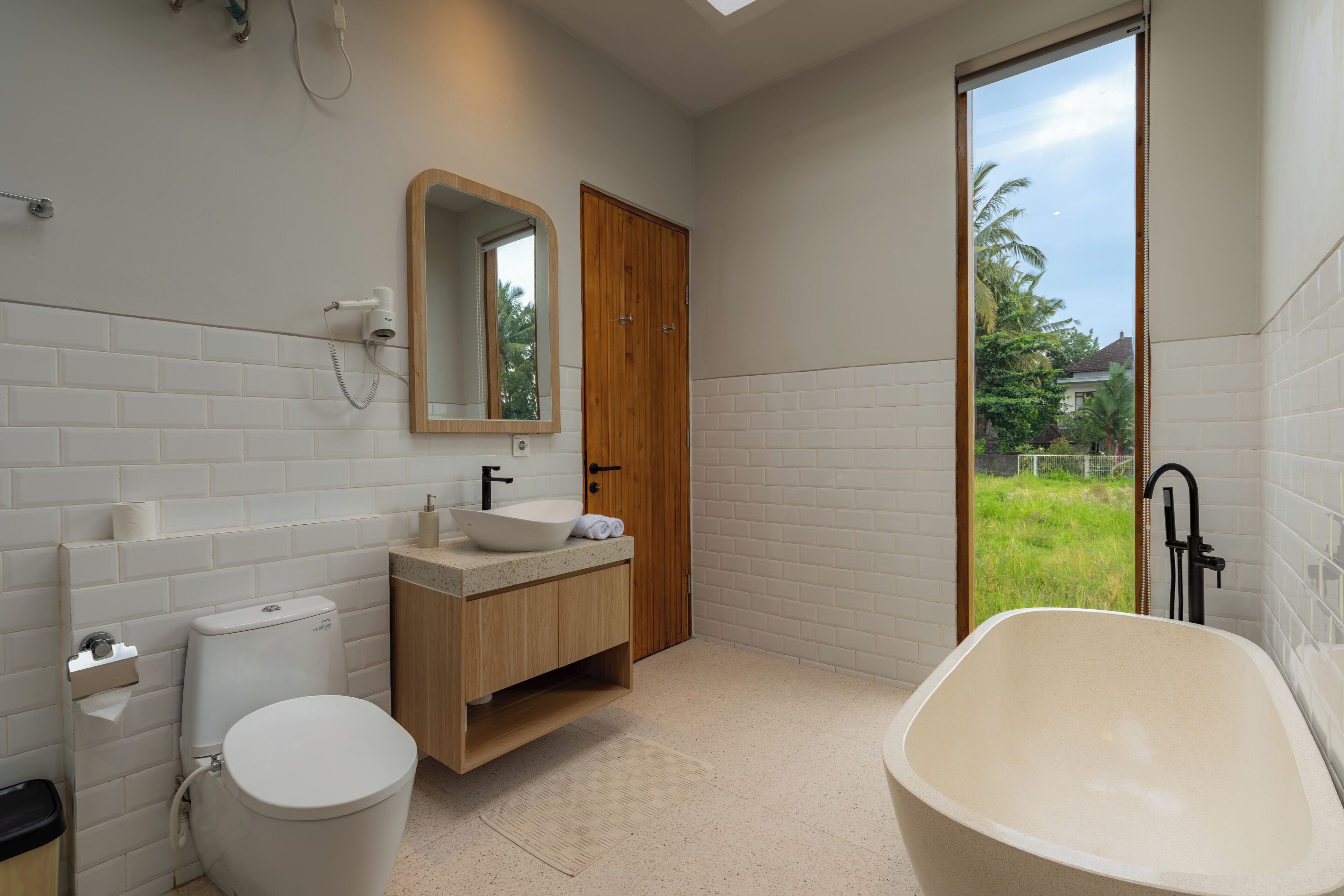 A modern bathroom with a toilet, sink, mirror, and bathtub.
