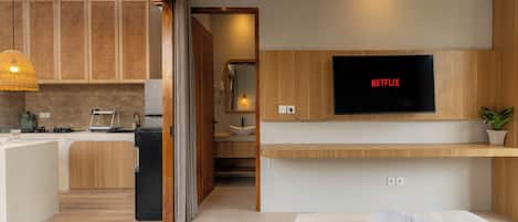 A modern hotel room with a kitchenette, a TV mounted on the wall, and a bed with a towel.