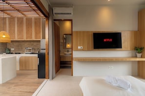 Ein modernes Hotelzimmer mit Küchenzeile, einem an der Wand montierten Fernseher und einem Bett mit Handtuch.